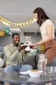 Smiling man receiving birthday cake from woman at home celebration with balloons - PhotoDune Item for Sale