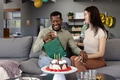 Couple celebrating birthday at home, man opening gift with joyful expression - PhotoDune Item for Sale