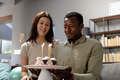 Celebrating birthday, couple smiling with cake and candles at home - PhotoDune Item for Sale