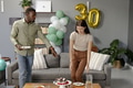 Celebrating birthday, friends arranging cake and decorations in cozy living room - PhotoDune Item for Sale