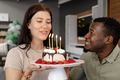 Celebrating birthday, woman holding cake with candles, man smiling beside her - PhotoDune Item for Sale