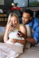 African American man proposing to surprised woman on couch at home, both smiling - PhotoDune Item for Sale