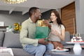 Couple exchanging gifts on sofa, smiling and celebrating birthday at home - PhotoDune Item for Sale