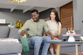 African American man opening gift bag on couch, celebrating birthday with friend - PhotoDune Item for Sale