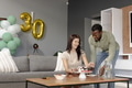 Celebrating birthday, couple enjoying cake and snacks in living room with balloons - PhotoDune Item for Sale