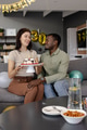 Celebrating birthday, woman presenting cake to smiling African American man on couch - PhotoDune Item for Sale