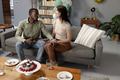 Couple sitting on sofa holding hands, celebrating with cake in living room - PhotoDune Item for Sale
