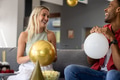 Friends laughing and holding balloons while celebrating at home on cozy sofa - PhotoDune Item for Sale