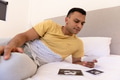 Young man relaxing on bed, looking at ultrasound photos with thoughtful expression - PhotoDune Item for Sale