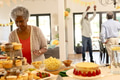 Elderly woman arranging cupcakes on table while guests celebrating in background - PhotoDune Item for Sale