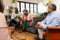 Elderly woman opening gift bag at home, surrounded by smiling friends - PhotoDune Item for Sale
