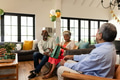 Elderly woman opening gift while celebrating with friends in cozy living room - PhotoDune Item for Sale