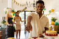 Serving cake at birthday party, man with friends celebrating in background - PhotoDune Item for Sale