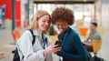 Two Smiling Female College Student Friends Checking Mobile Phone In Busy Communal Campus Building - PhotoDune Item for Sale