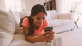 Young Girl Lying On Sofa In Lounge At Home Checking Social Media On Mobile Phone - PhotoDune Item for Sale