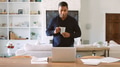Mature Man With Hot Drink Standing At Table At Home Reviewing Finances On Laptop - PhotoDune Item for Sale