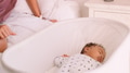 Close Up Of Mother Sitting On Bed Next To Sleeping Baby Son Lying In Cot In Bedroom - PhotoDune Item for Sale