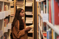 Teenage Asian Girl Browsing Bookshelves in Library and Reading Book - PhotoDune Item for Sale