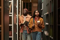 Young Black Man and Young Asian Woman Walking through Library Aisle Studying - PhotoDune Item for Sale