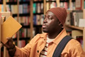 Young Black Man Selecting Book from Shelf in Library Setting - PhotoDune Item for Sale
