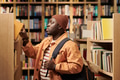 Young Black Man Searching Bookshelf in Library While Carrying Backpack - PhotoDune Item for Sale