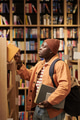 Young Black Man Searching Bookshelf in Library While Holding Textbooks - PhotoDune Item for Sale
