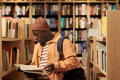 Young Black Man Reading Book While Standing between Library Shelves - PhotoDune Item for Sale