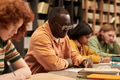 Young Black Man Writing Notes Beside Multiethnic Students in Library - PhotoDune Item for Sale