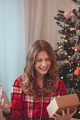 Young Woman Unwrapping Christmas Gift By Decorated Tree - PhotoDune Item for Sale