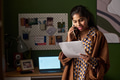 Young South Asian Woman Talking on Phone While Reading Document Indoors - PhotoDune Item for Sale