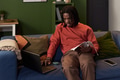 Young Black Man Studying with Notebook and Laptop While Sitting on Sofa - PhotoDune Item for Sale