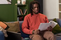 Young Black Man Sitting on Sofa Reading Documents in Living Room - PhotoDune Item for Sale