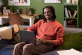 Portrait of Young Black Man Smiling While Using Laptop on Sofa - PhotoDune Item for Sale