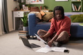 Young Black Man Sitting on Floor Reviewing Documents and Using Laptop - PhotoDune Item for Sale