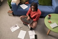 Young Black Man Typing on Laptop Surrounded by Papers in Living Room - PhotoDune Item for Sale