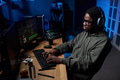 Young Black Man Wearing Headphones Coding on Computer in Dark Office - PhotoDune Item for Sale