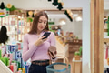 Young Woman Comparing Product Information Using Smartphone While Shopping - PhotoDune Item for Sale