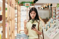 Young Asian Woman Shopping in Store While Using Smartphone for Browsing - PhotoDune Item for Sale