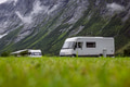 Motorhomes parked on a lush green meadow at the foot of steep rocky mountains with low clouds - PhotoDune Item for Sale