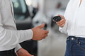 Young Caucasian woman buys a car at a dealership. Bearded man seller gives the car keys - PhotoDune Item for Sale