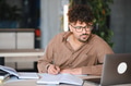 Focused arab university student taking notes while studying online with laptop - PhotoDune Item for Sale