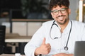 Smiling arab doctor showing thumbs up in medical office - PhotoDune Item for Sale