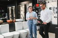 Salesman showing toilets to customer in bathroom fixtures store - PhotoDune Item for Sale