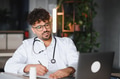 Arab doctor writing notes while looking at laptop in modern office - PhotoDune Item for Sale