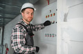 Electrician operating control panel wearing protective gear in building under construction - PhotoDune Item for Sale