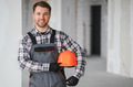 Construction worker holding helmet and smiling at construction site - PhotoDune Item for Sale
