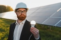 Engineer showing light bulb powered by solar panels in power plant - PhotoDune Item for Sale