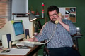 Caucasian Man Sitting at Desk Using Landline Phone and Computer - PhotoDune Item for Sale