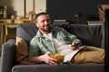 Man Relaxing on Sofa Watching Television and Eating Snacks - PhotoDune Item for Sale