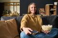 Young Adult Woman Watching Television While Eating Popcorn on Sofa - PhotoDune Item for Sale